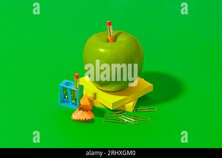 Granny Smith pomme placé sur des notes autocollantes près du bureau ou des fournitures scolaires sur fond vert vif Banque D'Images