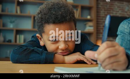 Paresseux non motivé fatigué épuisé fatigué petit écolier afro-américain écrivant des notes faisant des devoirs allongés sur la table. Ethnique enfant garçon enfant Banque D'Images