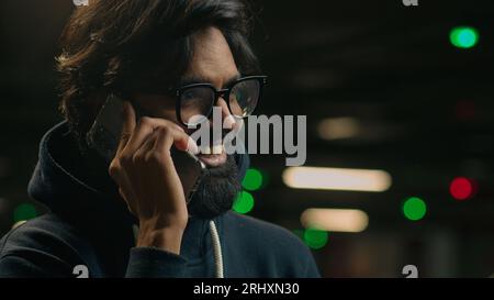 Gros plan homme indien barbu dans des lunettes au parking souriant homme adulte arabe homme dans des lunettes homme parler téléphone rire sourire agréable Banque D'Images