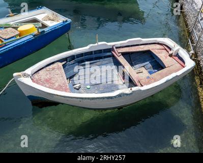 A small wooden row boat on water. The boat is tied on with white rope. Stock Photo