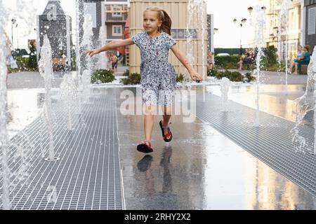 Le temps chaud de l'été. Enfant jouant dans la fontaine d'eau dans la ville. Fille heureuse jouant avec des arroseurs d'eau, courant et riant. Enfance active Banque D'Images