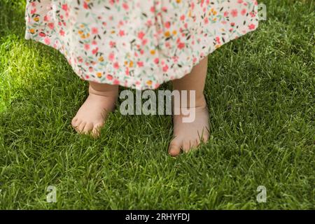 Petite fille apprenant à marcher sur l'herbe verte à l'extérieur, gros plan Banque D'Images