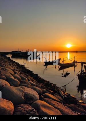 coucher de soleil sur la plage de paiton avec des silhouettes de bateaux de pêche ancrés dans le port Banque D'Images