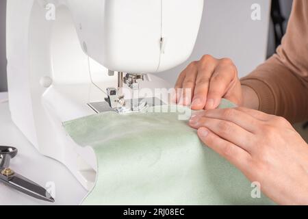 Tailleur mains couture tissu vert sur la machine à coudre moderne au lieu de travail dans l'atelier. Les mains des femmes cousent des morceaux de tissu sur la machine à coudre gros plan. Ha Banque D'Images