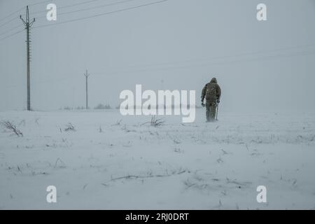 Silhouette de l'homme avec le détecteur de métal qui cherche sur le champ couvert de neige pendant le blizzard de neige Banque D'Images