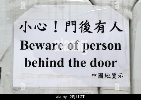 Avertissement bilingue, « attention à la personne derrière la porte », panneau aux travaux de construction sur le terrain de jeu Caine Road, niveaux intermédiaires, île de Hong Kong, 20 août 2023 Banque D'Images