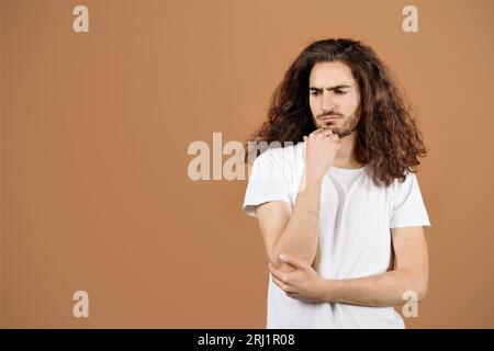 Portrait de Guy hispanique déprimé avec cheveux longs, fond beige Banque D'Images