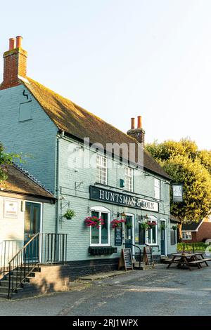 La maison publique du village 'Huntsman and Hornn' à Broomfield, Kent. bâtiment en briques vertes du 19e siècle avec paniers suspendus et tableaux de menu à l'extérieur. Banque D'Images