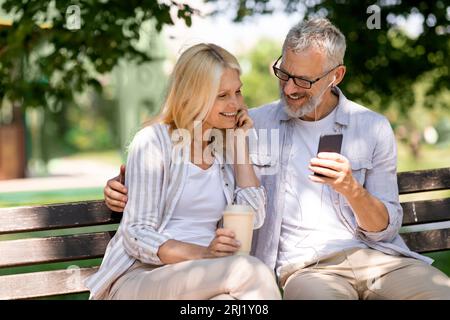 Couple plus âgé romantique avec smartphone se détendre sur Banc dans Summer Park Banque D'Images