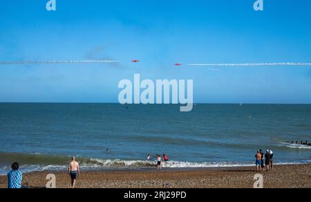 Les gens nagent dans la mer tandis que l'équipe de renommée mondiale de la RAF expose les Red Arrows le long du front de mer à l'Eastbourne Airbourne, un internati annuel Banque D'Images