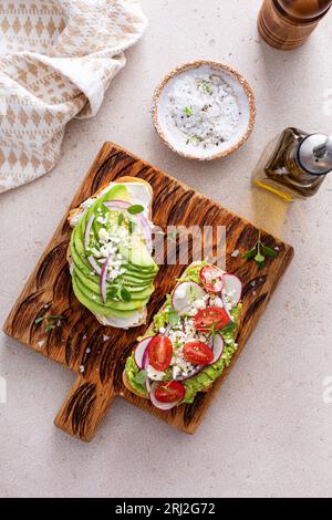 Toasts d'avocat avec radis, tomates et feta garnis d'huile d'olive, idée de petit déjeuner sain Banque D'Images