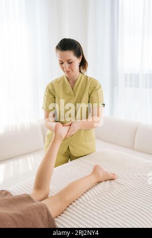 Portrait vertical de médecin orthopédique professionnel faisant des exercices orthopédiques de jambe de l'adolescente fille cliente, examinant et massant le patient Banque D'Images