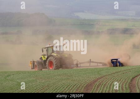 Un tracteur Claas Axion 850 Tractor Towing Dalbo Powerroll 1530 Rollers déclenche des nuages de poussière lorsqu'il tourne tout en roulant un champ d'orge de printemps Banque D'Images