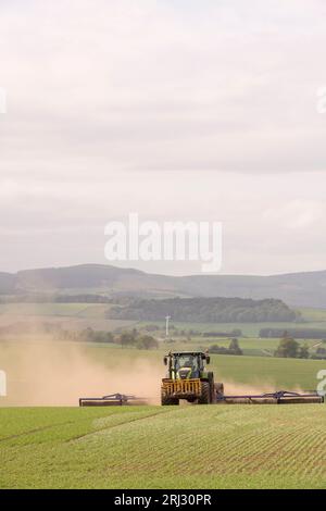 Un tracteur Claas remorquage Dal-bo Power-Roll 1530 Rollers Kicking Up Dust alors qu'il roule un champ d'orge de printemps sur des terres agricoles dans l'Aberdeenshire en mai Banque D'Images