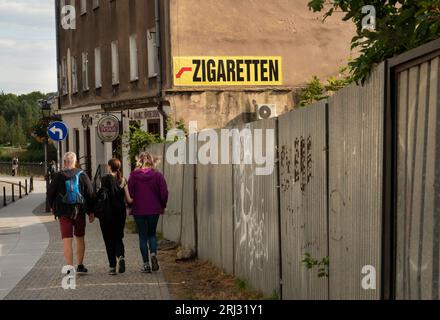 Zgorzelec, Pologne. 08 août 2023. 08.08.2023, Zgorzelec. Un panneau sur un pare-feu annonce l'achat de cigarettes dans un magasin de Zgorzelec, qui est situé à une centaine de mètres derrière la frontière germano-polonaise, un pont de la ville. Les touristes marchent à côté du panneau. Zgorzelec est le voisin polonais de la ville allemande de Goerlitz, sur l'autre rive de la rivière Neisse. Les cigarettes et l'alcool sont moins chers ici qu'en Allemagne. Crédit : Wolfram Steinberg/dpa crédit : Wolfram Steinberg/dpa/Alamy Live News Banque D'Images