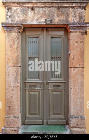 Belle porte avec des fenêtres en verre à un ancien manoir traditionnel avec linteau en pierre construit, dans la vieille ville d'Egine, sur l'île d'Egine, Grèce, Europe. Banque D'Images