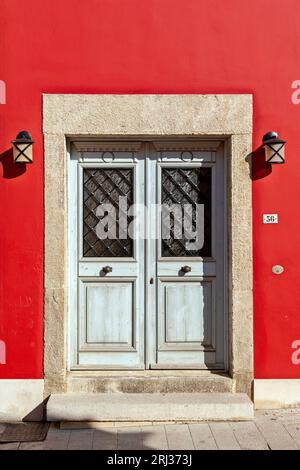 Incroyable entrée traditionnelle en bois avec portes doubles, deux lumières latérales et linteau en pierre et seuil, et un mur rouge vif, en Crète. Banque D'Images