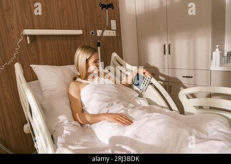 Jeune femme patient appuie sur les boutons sur le lit d'hôpital pour choisir une position confortable Banque D'Images