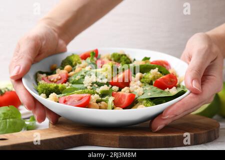 Repas sain. Femme mettant un bol de salade savoureuse avec du quinoa, des pois chiches et des légumes sur la table, gros plan Banque D'Images