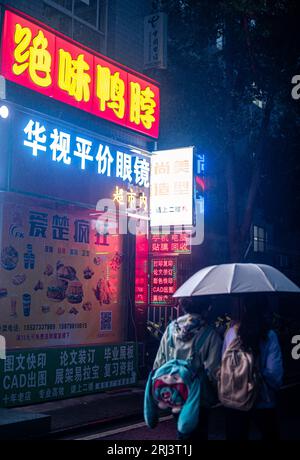 Une vue panoramique des gens marchant avec des parapluies dans les rues animées de Wuhan, Chine la nuit Banque D'Images