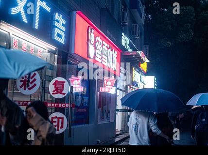 Une vue panoramique des gens marchant avec des parapluies dans les rues animées de Wuhan, Chine la nuit Banque D'Images