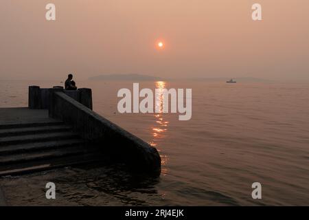 Seattle, Washington, États-Unis. 20 août 2023. Un couple observe le coucher de soleil sur les montagnes olympiques à travers la fumée de feu de forêt à Alki Beach Park. La qualité de l'air a considérablement diminué, car la fumée des feux de forêt dans la région a dégradé la qualité de l'air dans la ville à des niveaux insalubres. Crédit : Paul Christian Gordon/Alamy Live News Banque D'Images