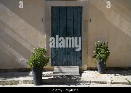 Entrée de la maison locale avec une porte en bois vert antique et des pots en argile avec des géraniums roses contre un mur de stuc fané sur la via Aleardi à Scicli Sicile, Banque D'Images