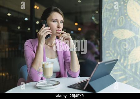 Une jeune femme d'affaires parle sérieusement et consciencieusement au téléphone dans un café, discute de questions importantes de l'entreprise Banque D'Images