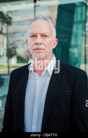 Portrait vertical d'un homme d'affaires sérieux mûr avec un costume exécutif, cheveux gris, et attitude réussie regardant pensif à la caméra. Travailleur d'entreprise homme confiant et bien habillé debout sur le lieu de travail. Photo de haute qualité Banque D'Images