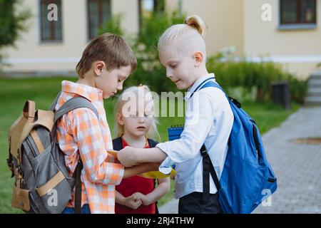 les enfants marchant de l'école avec des sacs à dos sur une journée ensoleillée ayant du plaisir à sauter des coups de pied les uns les autres. Début de l'année académique. Garçons près de la porte de l'école. Im Banque D'Images