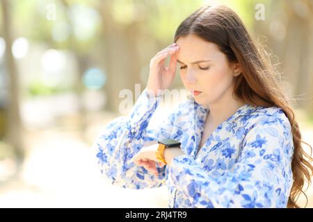 Femme inquiète vérifiant smartwatch marchant dans un parc ensoleillé Banque D'Images