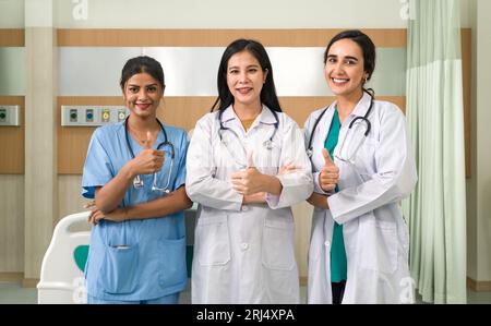 Un instantané de l'affirmation et du succès médical, mettant en vedette trois professionnelles de la santé donnant des pouces dans un cadre moderne de chambre d'hôpital. Banque D'Images