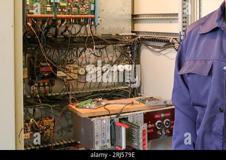Un électricien de travail masculin se tient devant un panneau électrique avec des fils, des transistors, des fusibles, des composants électroniques et des commutateurs. Banque D'Images