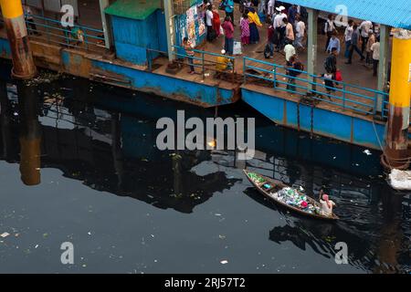 Un homme ramasse des déchets plastiques sur son petit bateau depuis la rivière Buriganga près de Sadarghat dans le vieux Dhaka, au Bangladesh. Banque D'Images