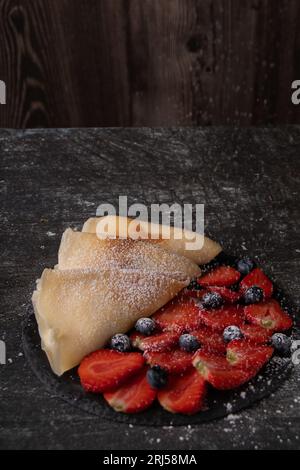 photo de fraises mûres et de myrtilles, crêpes frites et sucre en poudre saupoudré sur le dessus. sur fond gris Banque D'Images