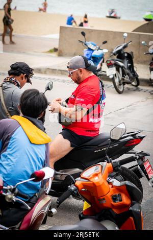 Un homme obtient son permis de conduire vérifié tout en conduisant sa moto le long de Beach Rd. Pattaya, Thaïlande. Banque D'Images