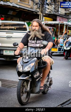 Un homme avec une très longue barbe fait son chemin le long de soi Buakhao, Pattaya, Thaïlande sur son scooter. Banque D'Images