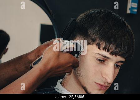 Un jeune garçon se faisant couper les cheveux par un coiffeur dans un salon de coiffure traditionnel Banque D'Images