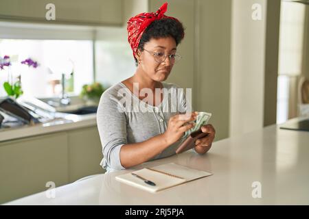 Femme afro-américaine comptant des dollars assis sur une table à la maison Banque D'Images