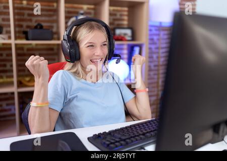 Jeune femme caucasienne jouant à des jeux vidéo portant des écouteurs célébrant surprise et émerveillée du succès avec les bras levés et les yeux fermés. con. gagnant Banque D'Images