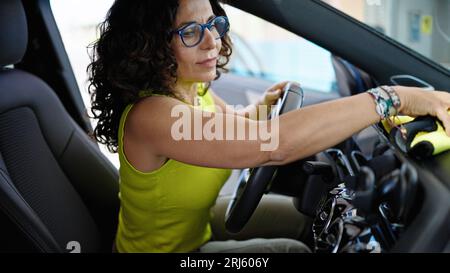 Femme hispanique d'âge moyen nettoyant l'intérieur de la voiture avec un chiffon en microfibre au poste de lavage de voiture Banque D'Images