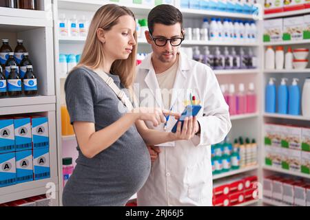 Homme et femme pharmacien et cliente enceinte regardant un écran de smartphone à la pharmacie Banque D'Images