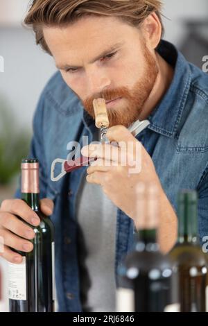 jeune homme décontracté reniflant le bouchon de la bouteille de vin Banque D'Images