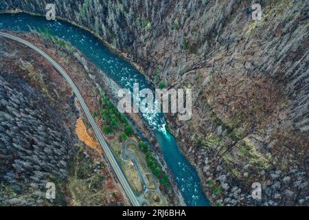 Une vue aérienne d'une rivière bleue sinueuse coulant à travers un long tronçon de route entouré de deux grandes collines rocheuses Banque D'Images