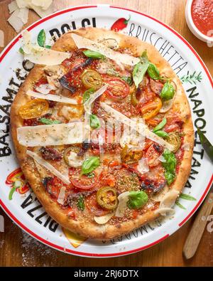 Une pizza fraîchement préparée servie sur une assiette blanche sur une table en bois, garnie d'une délicieuse sauce tomate Banque D'Images