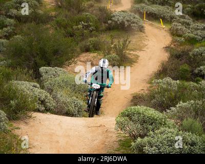 Un homme en équipement de protection complet monte son VTT sur un sentier escarpé Banque D'Images