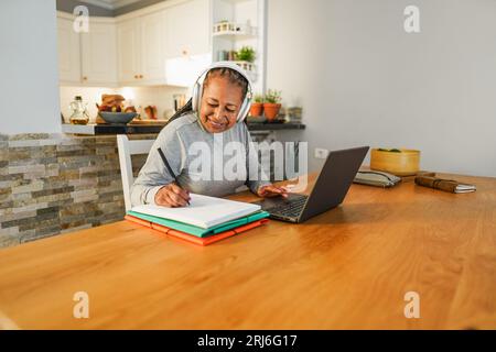 Femme africaine senior faisant webinaire de classe numérique de la maison - style de vie et concept de technologie des personnes âgées joyeuses - Focus sur le visage Banque D'Images