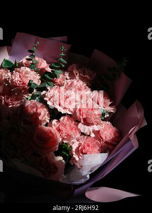 Un bouquet vibrant d'œillets roses et blancs et de roses disposées contre un ton noir Banque D'Images