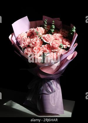 Un bouquet vibrant d'œillets roses et blancs et de roses disposées contre un ton noir Banque D'Images