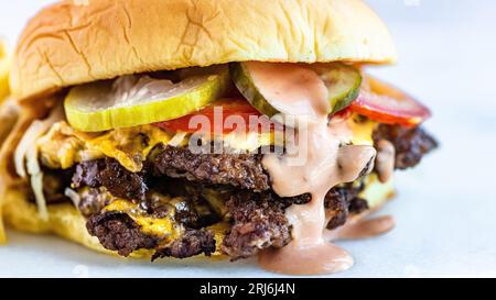 Gros plan d'un hamburger smash avec fromage, cornichons, tomates, vinaigrette ranch et frites. Banque D'Images